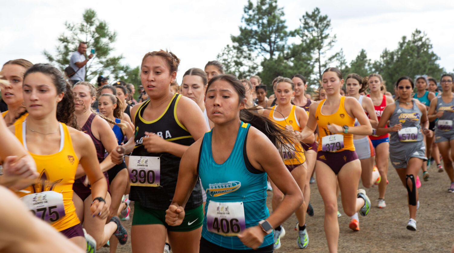 A large pack of female athletes racing cross country.