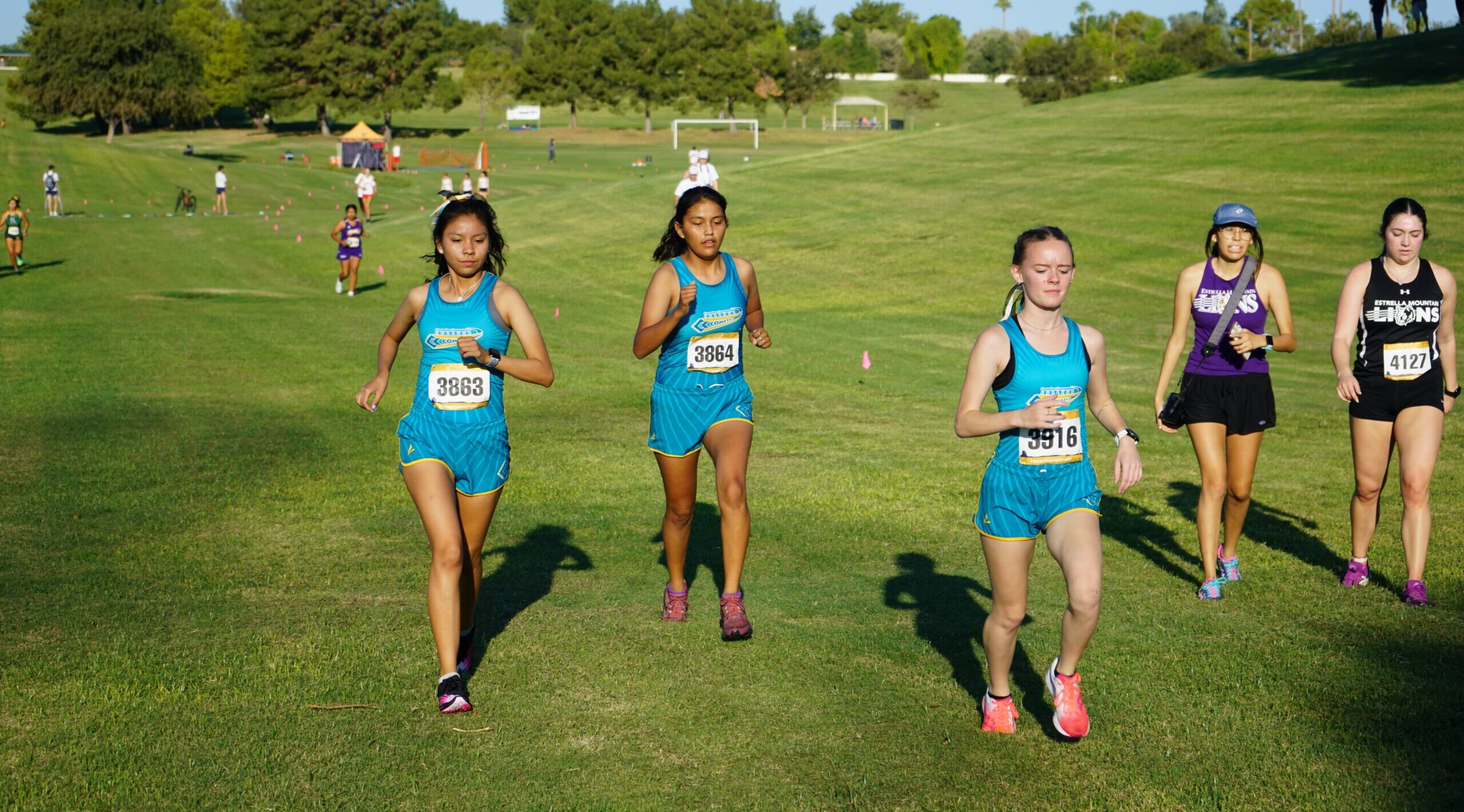 Three female runners striding out on a grass field.