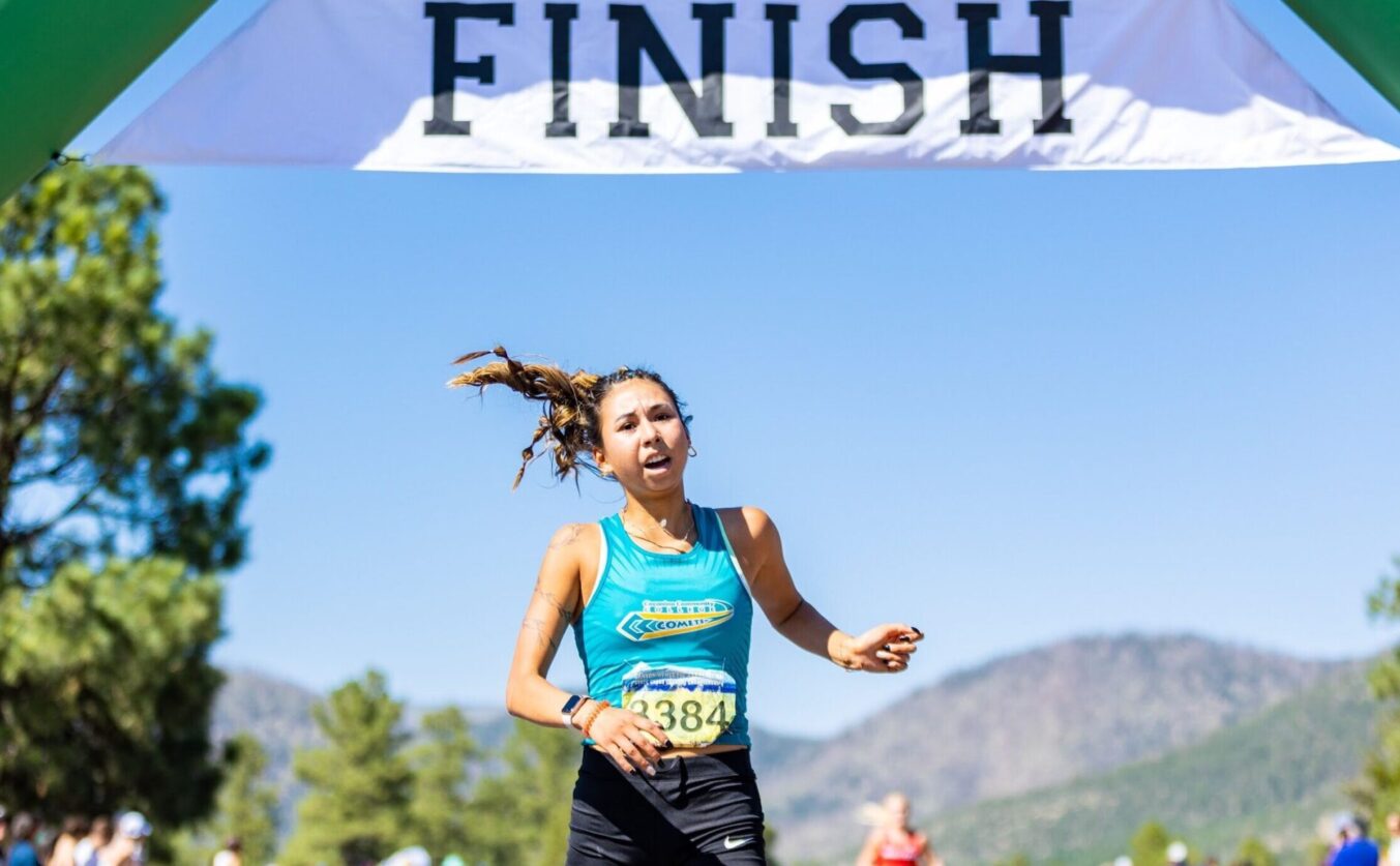 A female athlete crossing the finish line of a cross country race.