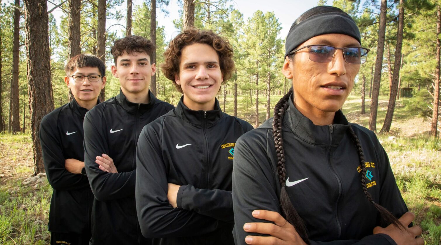 Four CCC male athletes posing in their warm ups with a forest background.