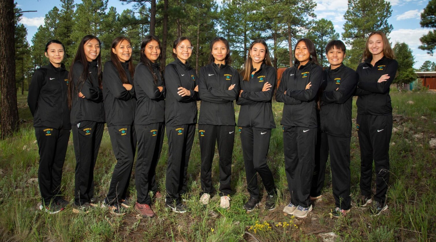 CCC's women's cross country team posing in their warm ups in the forest.
