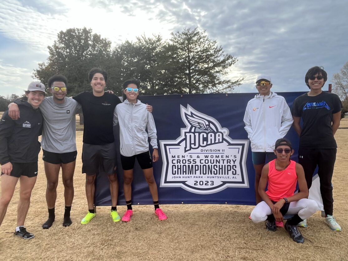 CCC's men's cross country team posing in front of a National Championship banner.