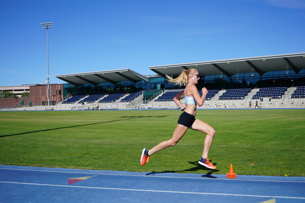 A runner in full stride while running around a blue track.