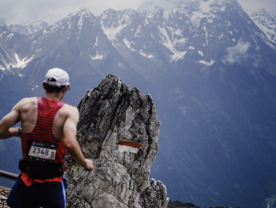 Athlete running running on trails with a mountain in the background.