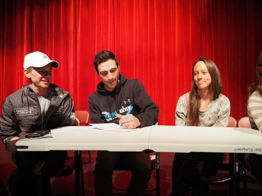 Three individuals sitting at a table signing a letter.