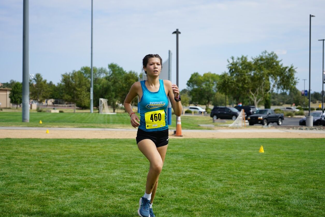 Female runner running across a grass field.